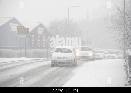 Autos fahren auf einer schneebedeckten Straße an einem Wintertag in Market Harborough, Leicestershire, Großbritannien. Stockfoto