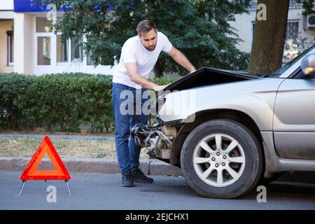 Fahrer Mann Blick auf zerstörte Auto in Autounfall. Mann bedauert über die Festsetzung Auto nach dem Autounfall. Tragische Autounfall. Gefährlicher Straßenverkehr situat Stockfoto