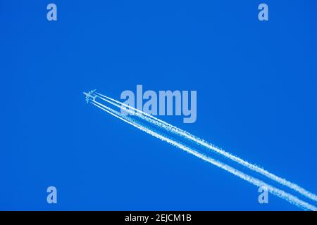 Hellblauer Himmel mit Kondensstreifen, die von einem Flugzeug hinterlassen werden, das an einem klaren Tag hoch über dem Himmel fliegt Stockfoto