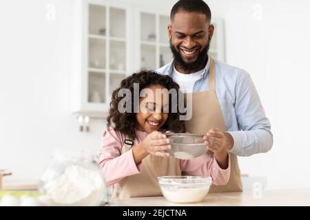 Fröhlicher schwarzer Mann und seine Tochter, die Teig zubereitet Stockfoto