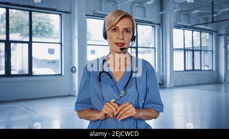 Reifer Arzt im Headset und Uniform sprechen bei der Kamera während Beratung Stockfoto