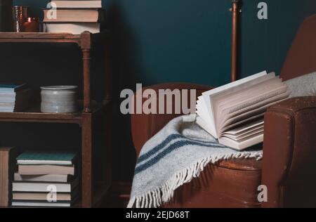 Landschaftsbild des Wohnraums. Ein Buch ruht auf einem alten Lederstuhl mit Büchern und Gegenständen, die im Hintergrund in Regalen zu sehen sind. Heimbüro, c Stockfoto