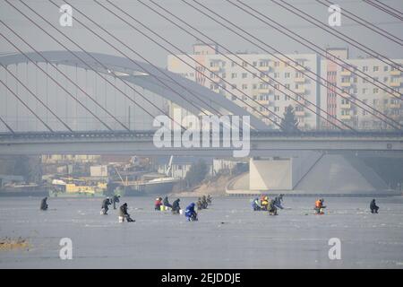 Blick auf Menschen, die auf dem gefrorenen Motlawa-Fluss gegen eine Kabelbrücke in Danzig, Polen, fischen Stockfoto