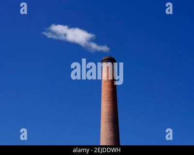 Rauch steigt aus einem Industrieschornstein vor einem klaren blauen Himmel in einer ruhigen Umgebung auf Stockfoto