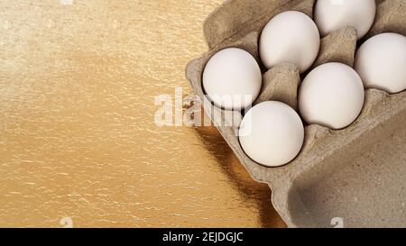 Weiße Hühnereier in einem Papptablett auf goldenem Hintergrund. Hintergrund mit Platz für Text. Gesundes Essen und Osterkonzept. Eiweißfutter Stockfoto