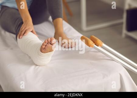 Frau mit einem gebrochenen verputzten Bein sitzt auf einer Couch nach der ersten Hilfe nach einem Unfall. Stockfoto