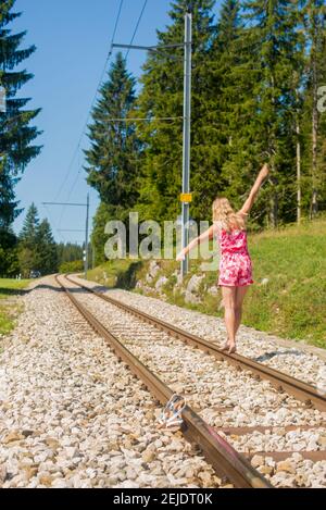 Ein kleines Mädchen, das auf einer Eisenbahnstrecke mit Bäumen reitet Im Hintergrund Stockfoto