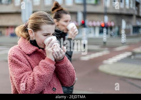 Junges Mädchen und ihre Mutter trinken heißes Getränk aus Papier Tassen auf der Straße im Winter Stockfoto