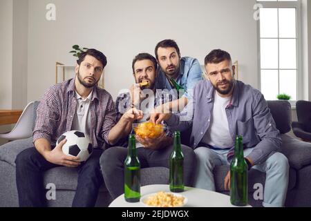 Männer schauen sich ein wichtiges Fußballspiel an, bei dem Chips und Bier zu Hause vor dem Fernseher sitzen. Stockfoto