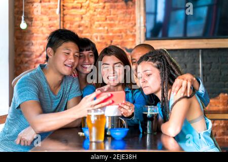 Eine Gruppe internationaler Freunde, die über Inhalte auf einem Smartphone-Bildschirm lachen. Stockfoto