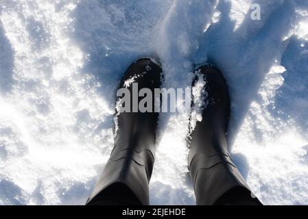 Schwarze Gummistiefel im Schnee, von oben geschossen. Stockfoto