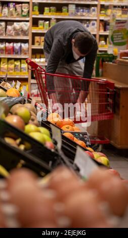 Ein Mann mit einem Einkaufswagen hinter einem Obststand in einem Bio-Lebensmittelgeschäft. Obst und Gemüse ohne Plastikfolie auf dem Display. Stockfoto