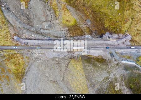 Glen Croe, Arrochar, Schottland, Großbritannien. Februar 2021, 22. Luftaufnahme von Erdrutschpräventivarbeiten zu A83 in Ruhe und sei dankbar Pass in Glen Croe. Die wichtige Route wurde von Erdrutschen geplagt, die oft die Hauptfahrbahn A83 gesperrt haben und den Verkehr dazu zwingen, die einspurige alte Militärstraße unten zu benutzen. Die letzten Erdrutsche haben diese Straße sogar blockiert. Derzeit wird der Verkehr in Konvois einbahnig begleitet. PIC; Konvoi auf der alten Militärstraße an der neuen Mauer. Iain Masterton/Alamy Live News Stockfoto