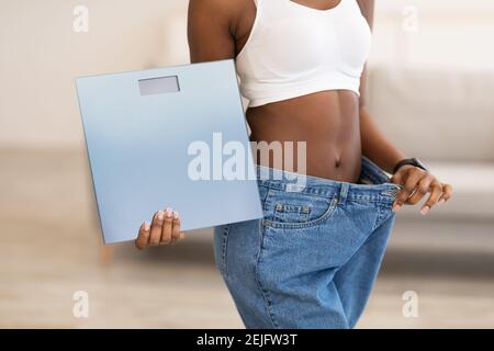 Slim Woman Holding Waagen Tragen Große Jeans Nach Dem Slimming Indoors Stockfoto