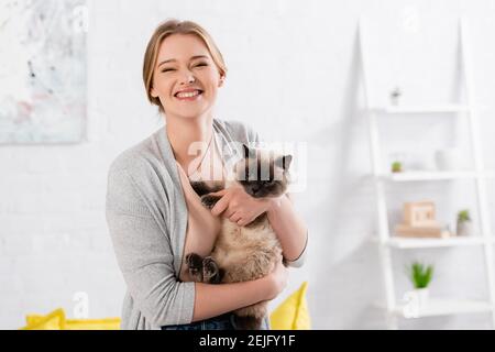 Glückliche Frau, die die Kamera anschaut, während sie die siamkatze hält Stockfoto