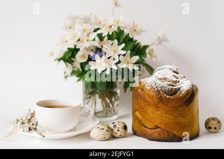 Osterkarte. Ein Kuchen, eine Tasse Tee, Primeln in einer Vase und Wachteleier auf hellem Hintergrund Stockfoto