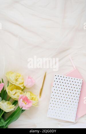 Ein Rand von rosa Blüten von gelben Tulpen, Accessoires und Kosmetik auf dem Hintergrund. Grundriss Büro für Damen. Flach liegend, Draufsicht. Stockfoto