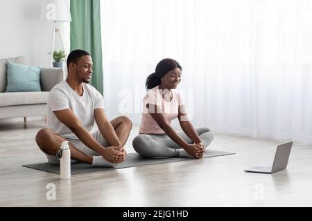 Fröhliche afroamerikanische Paar mit Online-Yoga-Klasse Stockfoto