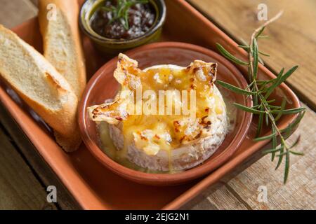 Französischer Camembert, der in einem Ofen mit Trüffel-, Knoblauch- und Honigsoße gebacken wurde, serviert mit geröstetem französischem Brot und karamellisiertem Zwiebelchutney Stockfoto