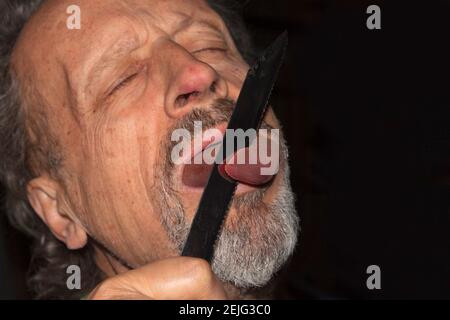 Großvater erschreckt seine Enkel an Halloween, schneidet ihm mit einem Messer eine Rindzunge in den Mund Stockfoto