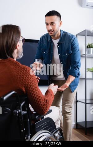 Junger hispanischer Mann, der einem behinderten Vater Wasser und Pille gibt Bei unscharfem Vordergrund Stockfoto