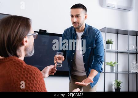 Junger hispanischer Mann, der Glas Wasser und Pille gab Papa auf verschwommenem Vordergrund Stockfoto
