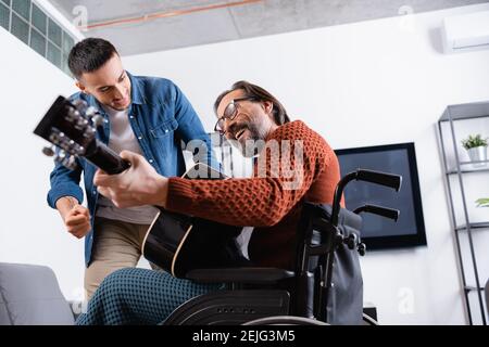Low-Angle-Ansicht der fröhlichen behinderten Mann spielt Gitarre in der Nähe Aufgeregt hispanischen Sohn Stockfoto