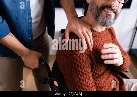 Teilansicht des Mannes, der die Schulter des freudvollen behinderten Vaters berührt Stockfoto