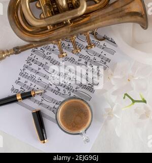 Schwarze Kaffeetasse auf einer Partitur mit Trompete und Blume Stockfoto