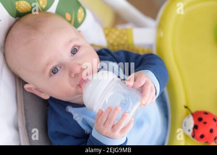 Lächelndes, 7 Monate altes Baby, das die Wasserflasche im Liegen hält Stockfoto