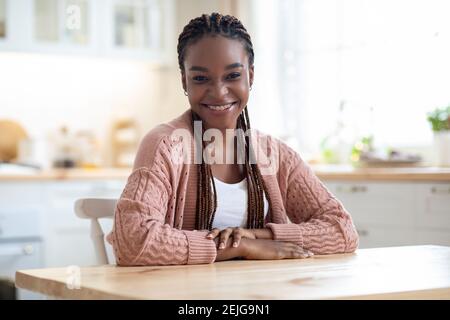 Porträt Einer Fröhlichen Jungen Afroamerikanischen Frau, Die Am Tisch Sitzt In Der Küche Stockfoto