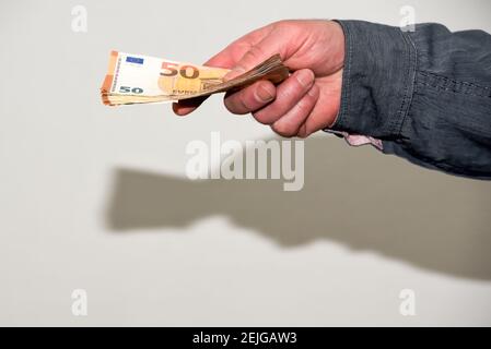 Ausgestreckte männliche Hand gibt einen Wad von Euro-Banknoten. Arbeit und Geschäfte in der nicht angemeldeten Wirtschaftstätigkeit der Schattenwirtschaft Stockfoto