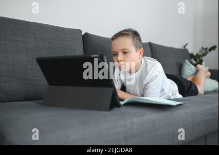 Online-Bildung, Homeschooling. Schuljunge mit Online-Unterricht zu Hause auf dem Trainer Stockfoto
