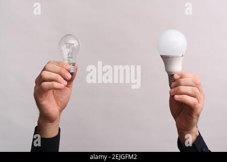 In den männlichen Händen eine LED-Lampe und eine Glühbirne. Das Konzept der Energieeinsparung. Stockfoto