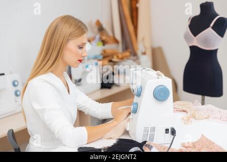 Modische Geschäft, Frau näht Kleidung auf Nähmaschine. Lächelnde Schneiderin weibliche Arbeit in der Werkstatt. Stockfoto