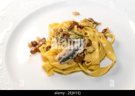 Tagliatelle mit le Sardinen - sizilianische Pasta mit Rosinen, Pinienkernen und Fenchel, close up in weißer Schale Stockfoto