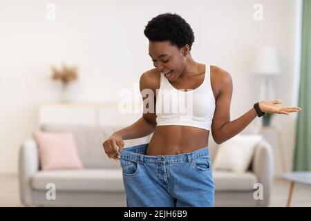 Aufgeregt Schlanke Afrikanische Frau Trägt Übergroße Hose Nach Gewichtsverlust Indoor Stockfoto