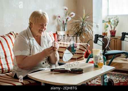 Ältere Schönheit und Hautpflege. Ältere ältere Menschen plus Größe blonde Frau mit Behinderung Anwendung Lippenstift in der Nähe des Spiegels zu Hause. Stockfoto
