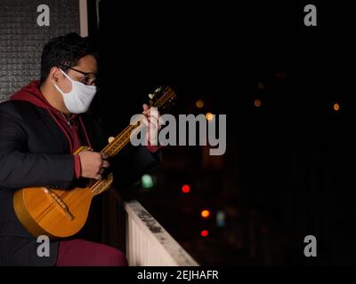 Mann in einer Maske spielt Gitarre auf dem Balkon von Sein Haus - das Konzept der Covid-19 Quarantäne Stockfoto