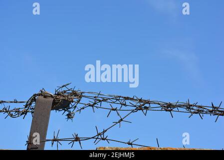 Schwarzer Metallzaun mit Stacheldrähten gegen Diebe am blauen Himmel. Stockfoto