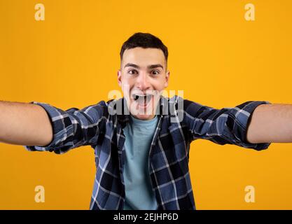 Glücklich Millennial Kerl nimmt Selfie auf orangen Studio Hintergrund Stockfoto