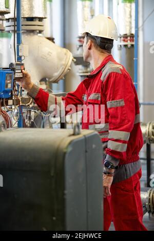 Thema der Energiewirtschaft: Ein Techniker in roten Overalls und weißem Helm überprüft Heizungsparameter an Thermometern. Wartung und Inspektion. Stockfoto