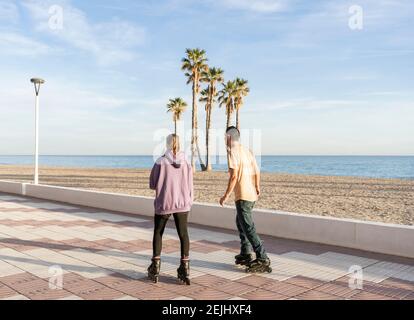 Junges Paar Rollschuhlaufen in Promenade am Meer mit Palmen im Hintergrund.Rückansicht von Sport und Fitness Lifestyle Konzept mit Kopierraum Stockfoto