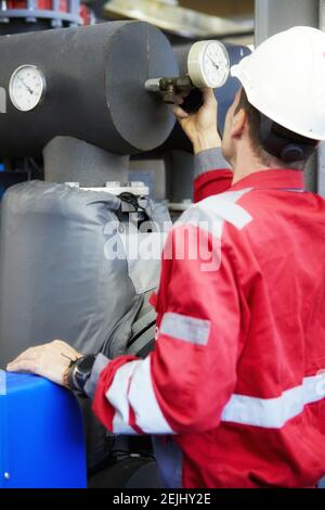 Thema der Energiewirtschaft: Ein Techniker in roten Overalls und einem weißen Helm, der die Heizungsparameter überprüft. Heizwasserverteilungstechnik. Stockfoto