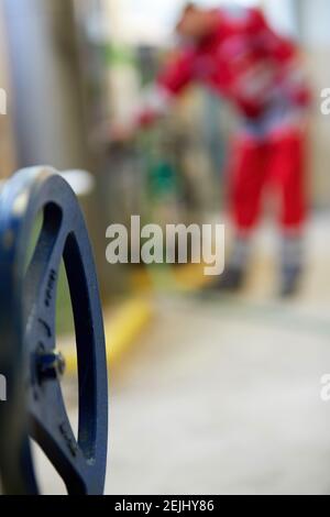 Thema der Energiewirtschaft: Ein Techniker in roten Overalls und einem weißen Helm, der die Heizungsparameter überprüft. Heizwasserverteilungstechnik. Stockfoto