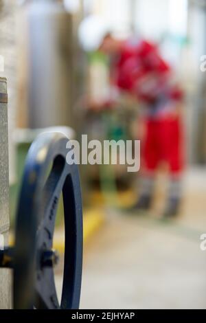 Thema der Energiewirtschaft: Ein Techniker in roten Overalls und einem weißen Helm, der die Heizungsparameter überprüft. Heizwasserverteilungstechnik. Stockfoto