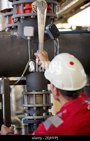 Thema der Energiewirtschaft: Ein Techniker in roten Overalls und einem weißen Helm, der die Heizungsparameter überprüft. Heizwasserverteilungstechnik. Stockfoto