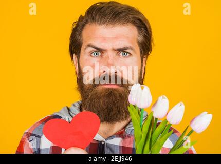 Valentinstag. Ernster Mann mit rotem Herz und Blumen. Valentine Geschenke mit Liebe. Stockfoto