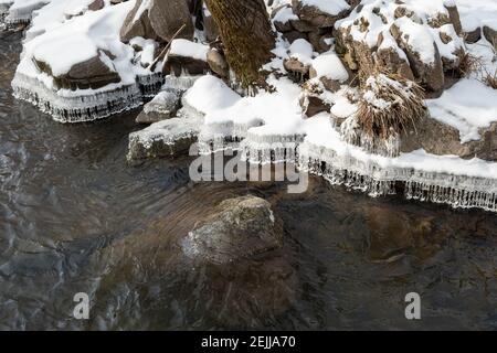 Erstaunliche Kristall Eiszapfen Formen hängen von der Kante des Schnees Überdachtes Flussufer im Winter Stockfoto