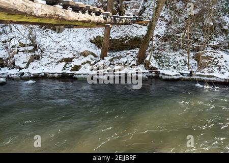 Hängende Holzbrücke, erstaunliche Formen von Eiszapfen am Flussufer und schneebedeckte Landschaft Stockfoto